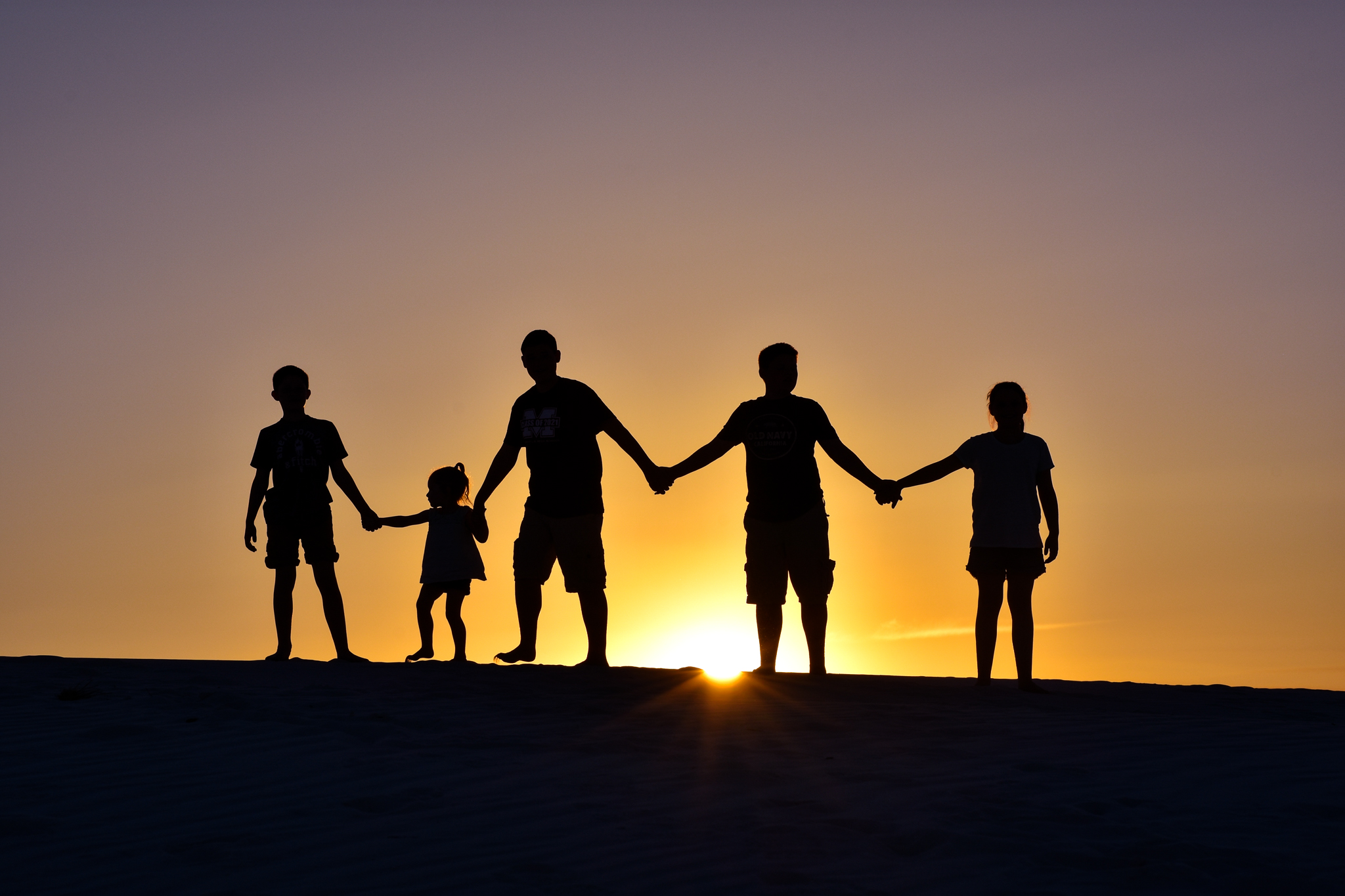 Silhouette of five kids with the sun setting behind the dunes at White Sands