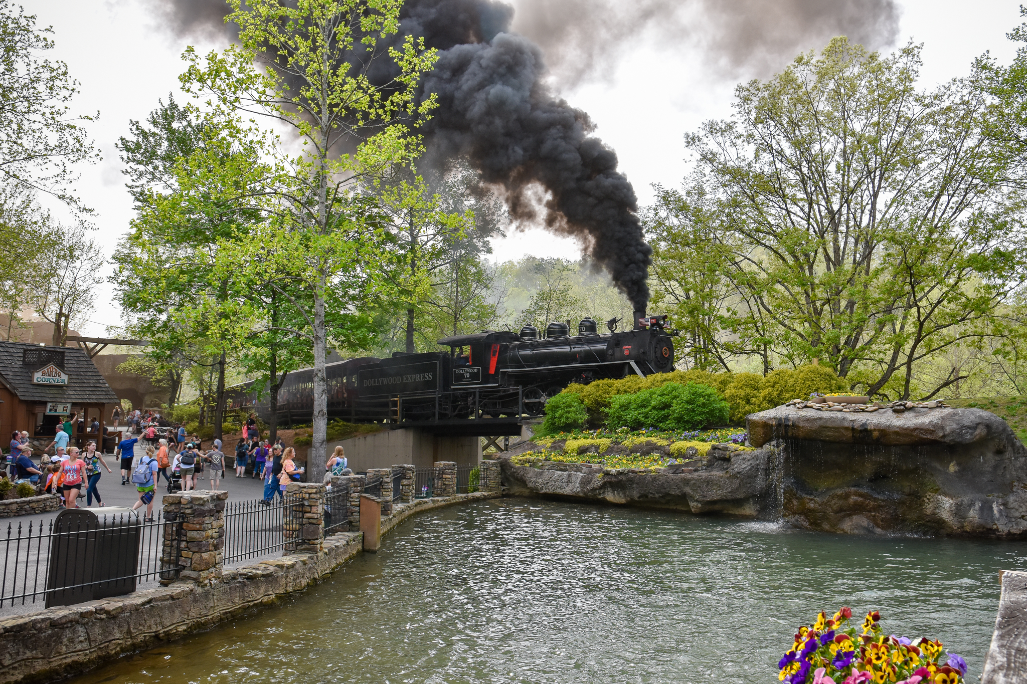 The Dollywood Express (big black train) running through Dollywood with billowing black smoke, amidst the green trees and flowers.
