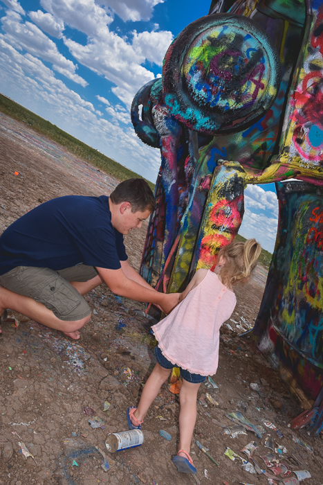 Teen boy and young girl spray painting a car at Cadillac Ranch