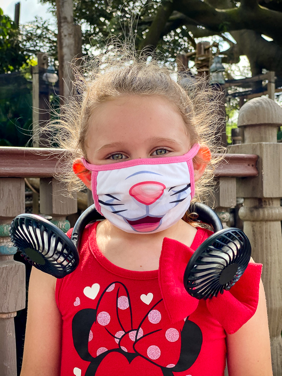 Masked girl using personal fan to stay cool at WDW
