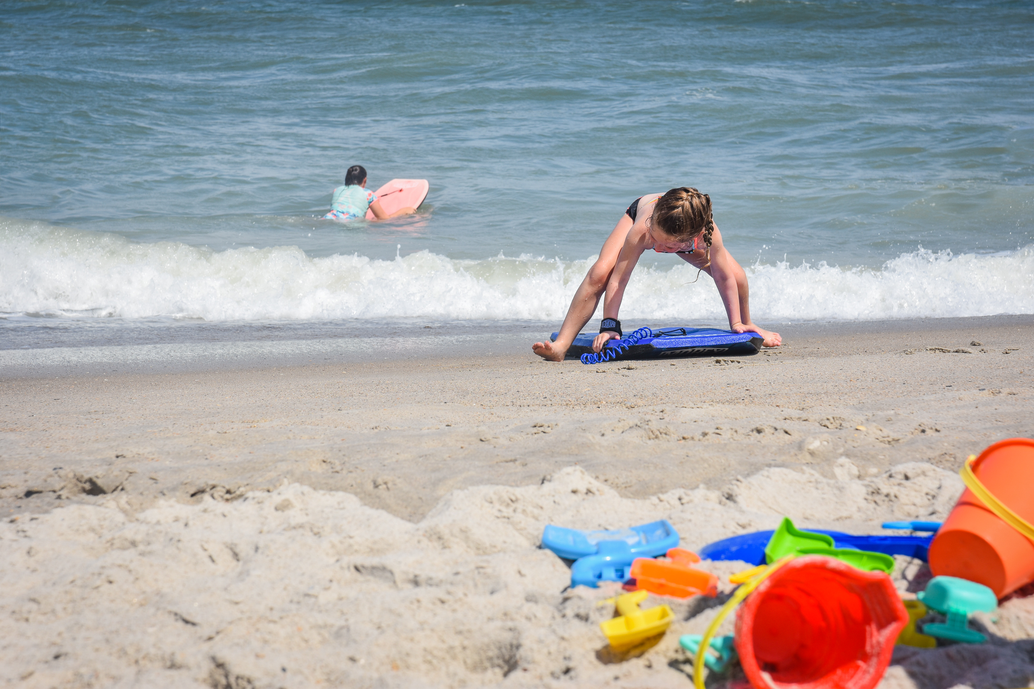 Girls playing in the water at the beach and on the sand with bodyboards and beach toys
