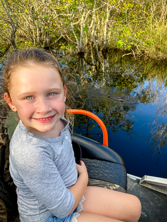 Smiling girl on airboat near an alligator in the Everglades