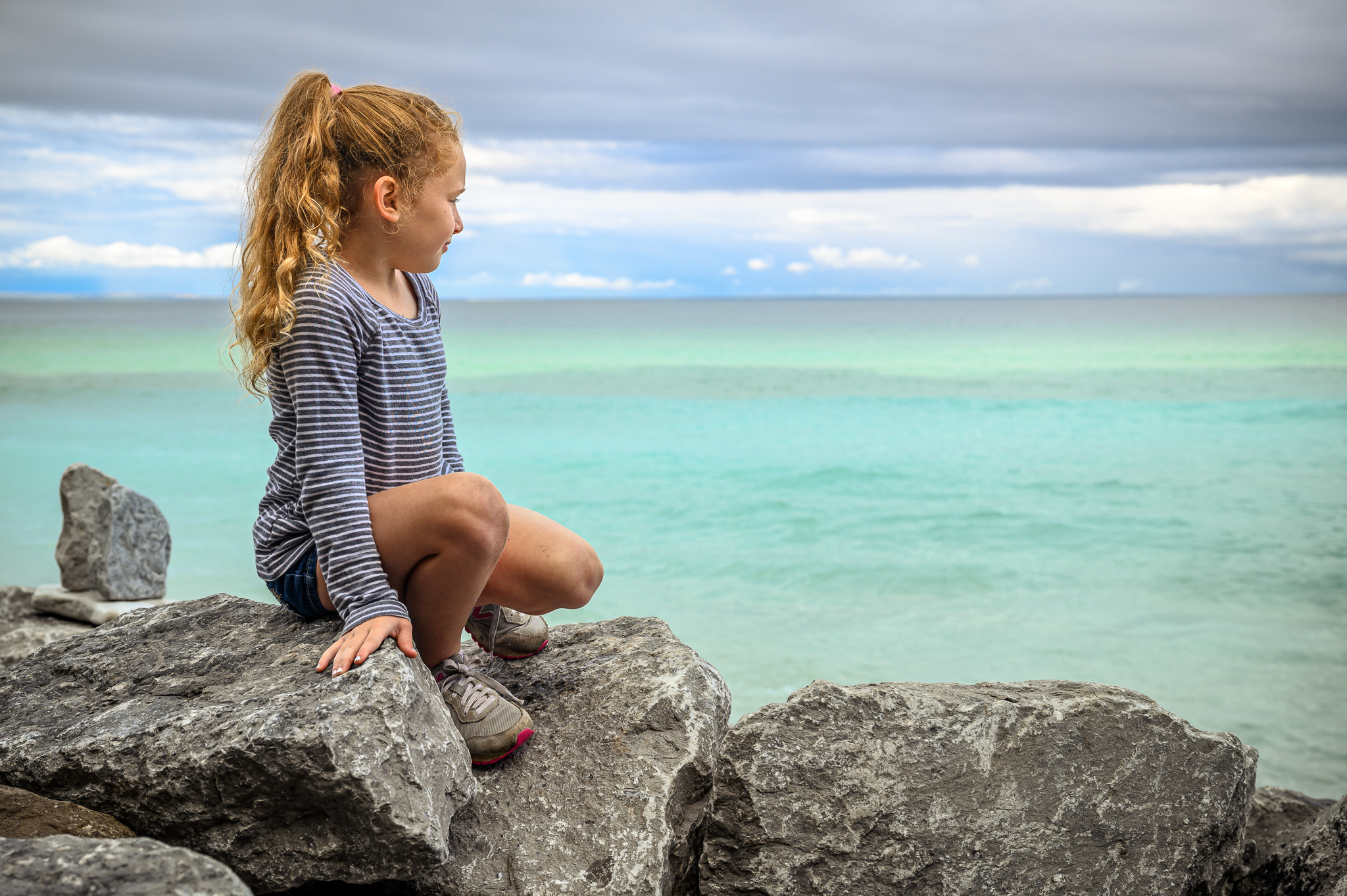 girl sitting on the rocky shore of the turquoise blue Lake Huron on Mackinac Island